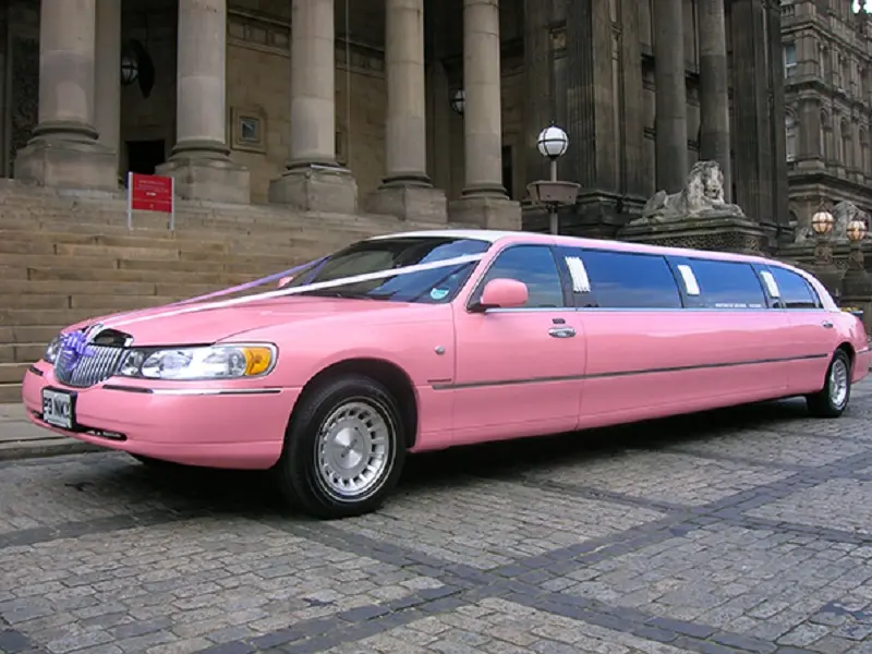 A vibrant pink limousine with a professional chauffeur ready for a wedding hire.